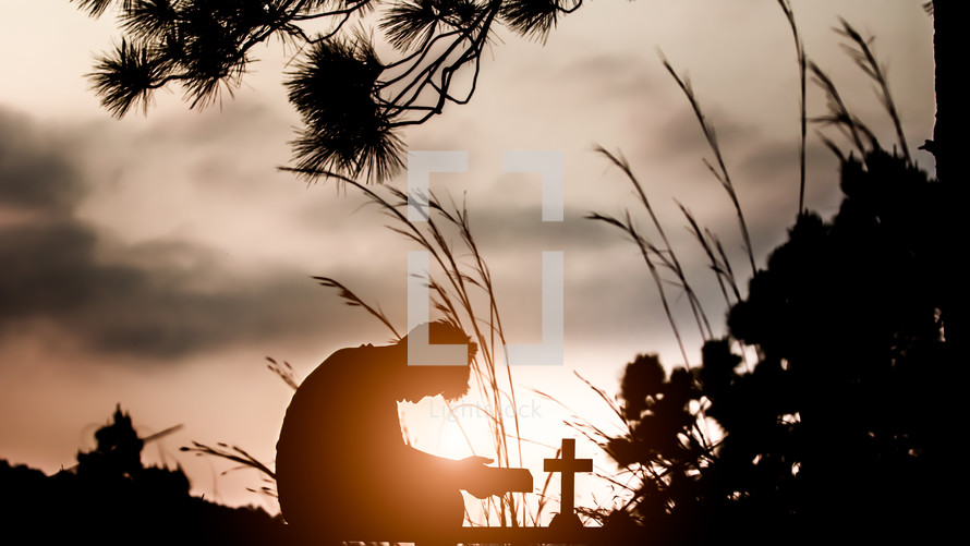 silhouette of a boy with a cross praying outdoors 