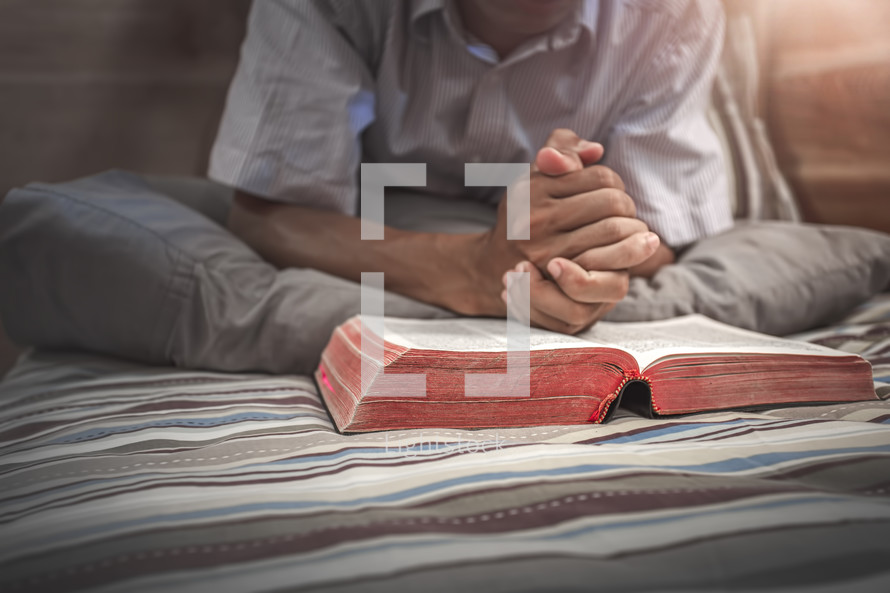 a man praying over a Bible in bed 