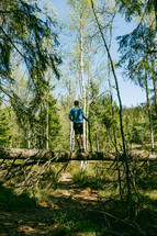 a man standing on a fallen tree in a forest 