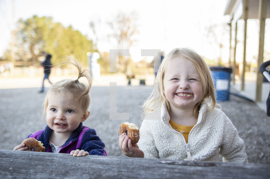 Two little girls eating a donut and smiling