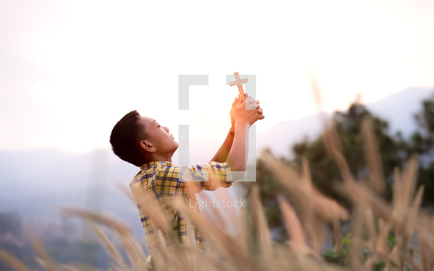 a young man holding a cross praying in a field 