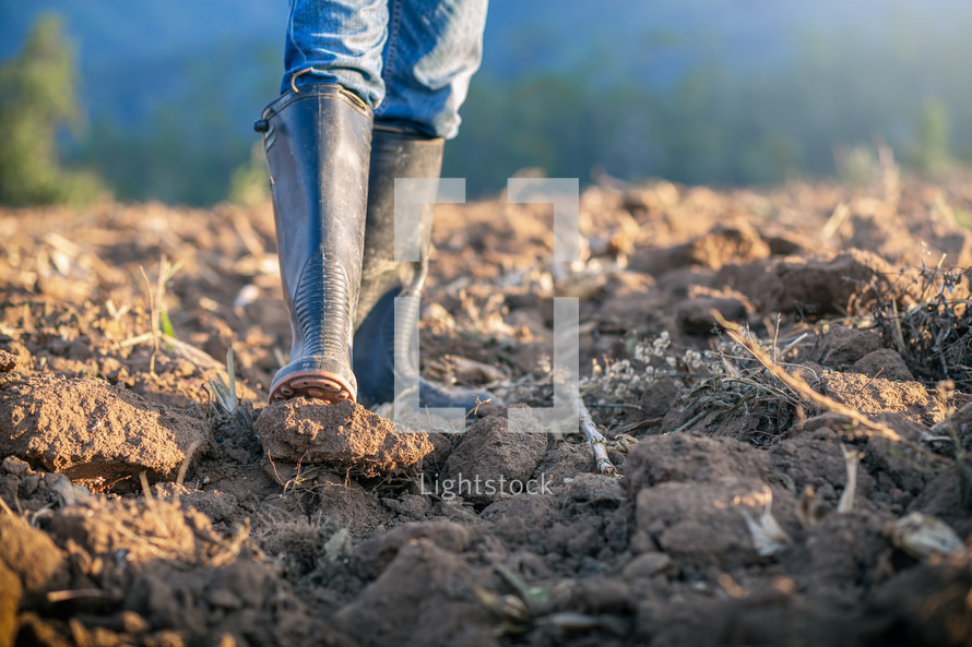 man with rubber boots tilling soil 