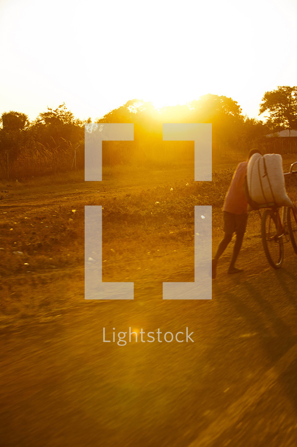 A man pushing a bicycle in Malawi, Africa under intense sunlight. 