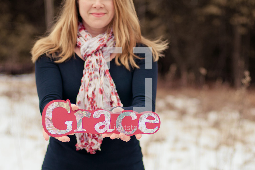 Woman standing outside in the snow holding a grace sign.