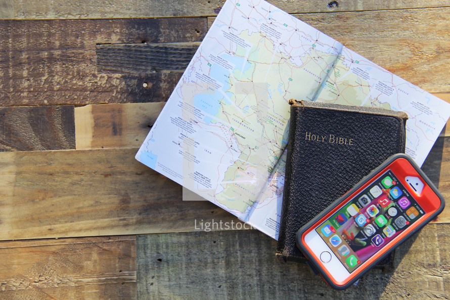 map, Holy Bible, and cellphone on a wood floor 