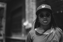 face of an African American woman in a ball cap and sunglasses 