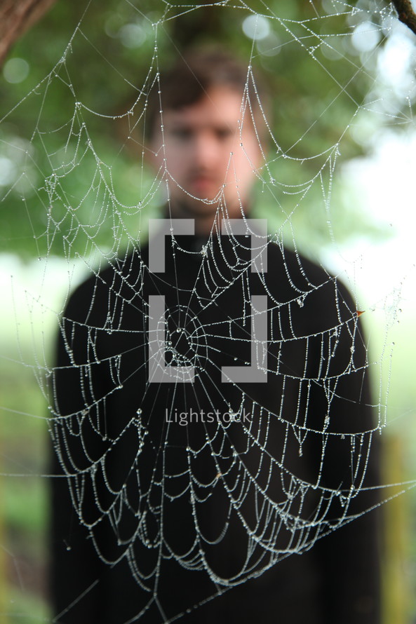 man standing behind a wet spider web
