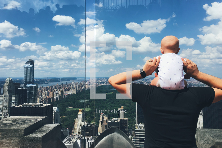 baby in a onesie on dad's shoulders taking in the view of a city 
