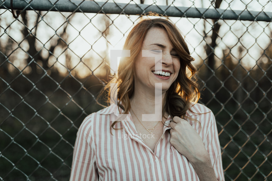 A laughing woman standing in front of a chain link fence.