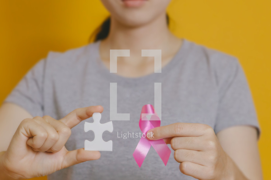 holding a pink ribbon and puzzle piece 