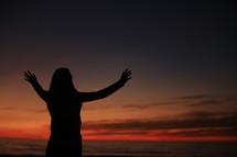 Woman with arms raised at sunset