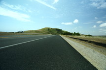 looking down the highway at a grass covered hill
