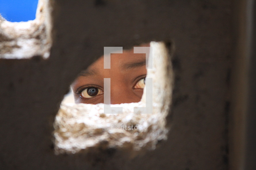A child peeking through a hole in a wall.
