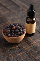 Bowl Full of Dried Juniper Berries on a Wooden Table and essential oil bottle 