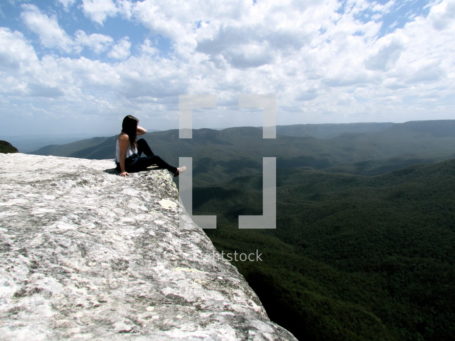 woman sitting on the edge of a cliff looking out 
