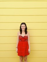 smiling woman in a red dress against a yellow wall 