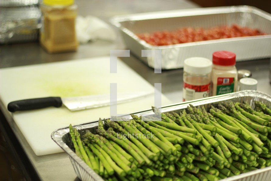 asparagus in a tray and knife on a cutting board in a kitchen 