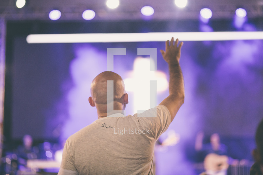 man standing with hand raised at a worship service 
