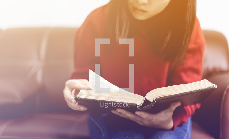 a woman reading a Bible sitting on a couch 