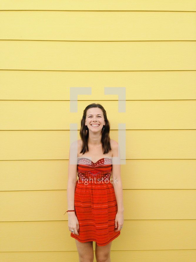 Smiling woman standing against a yellow paneled wall.