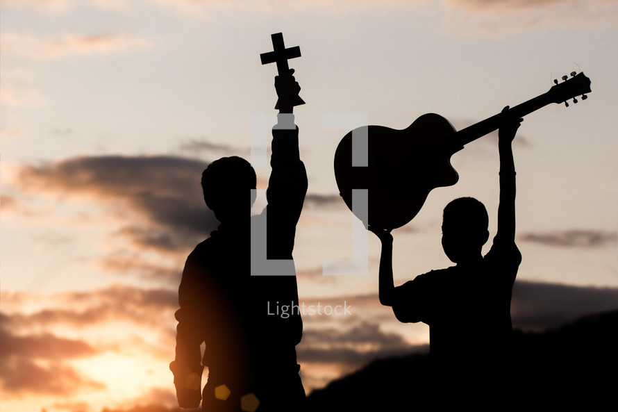 silhouettes of two boys at sunset one with a guitar and the other with a cross 