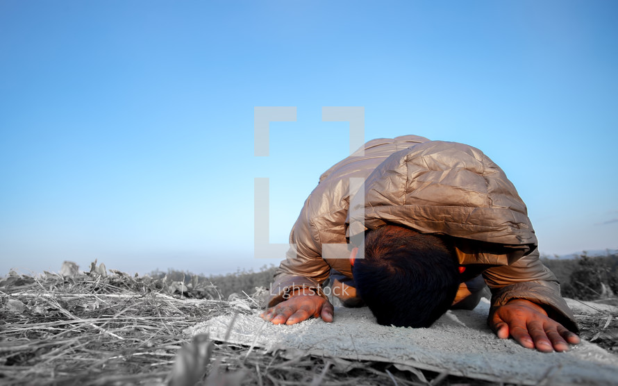 a man kneeling in praying on a rug outdoors 