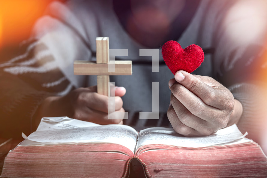 a man holding a cross and red felt heart over the pages of a Bible 