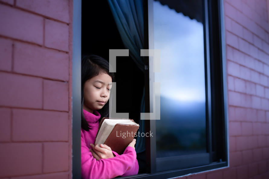 a girl child praying in an open window during quarantine 