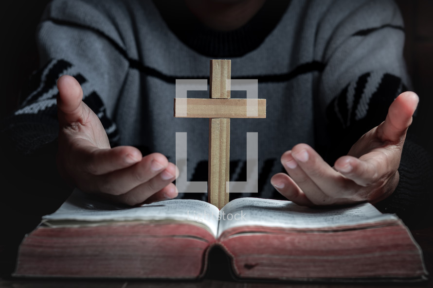 a man with a cross and hands in prayer over a Bible 