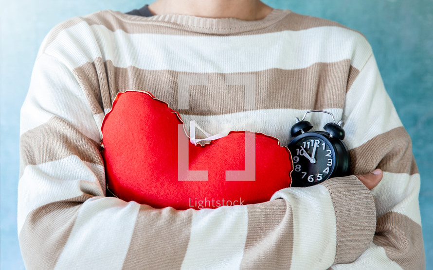 person Hugging a red heart and alarm clock, valentine day background.