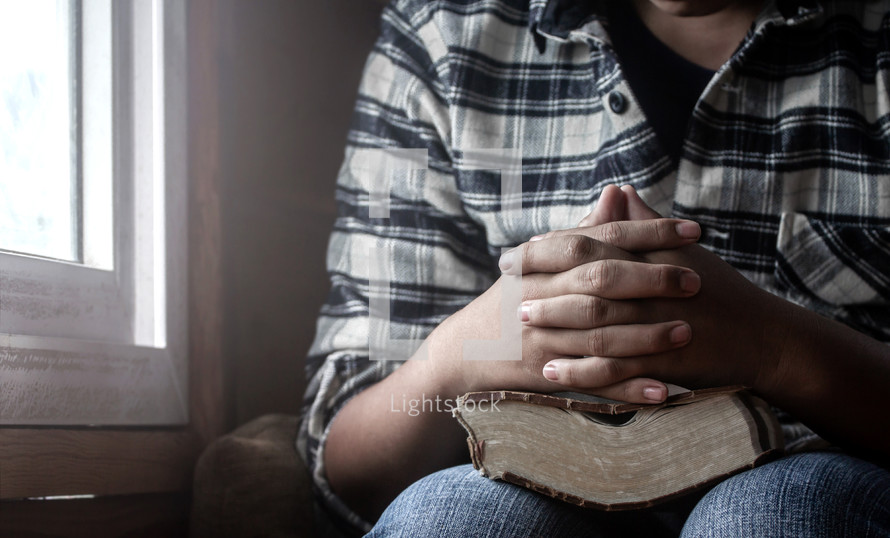 praying hands over a Bible in a lap 