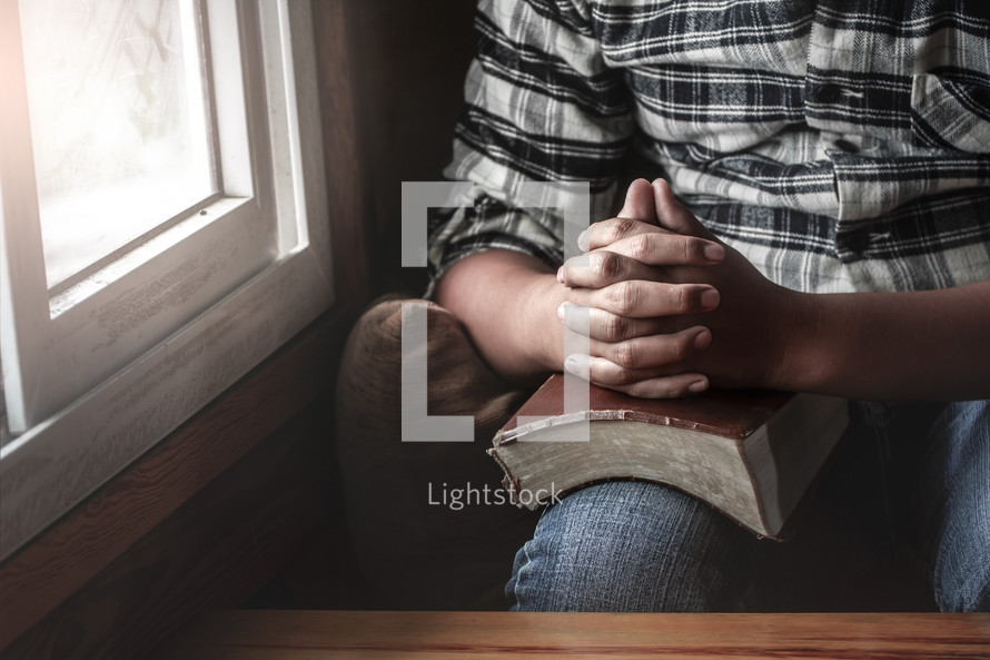 praying hands over a Bible in a lap 
