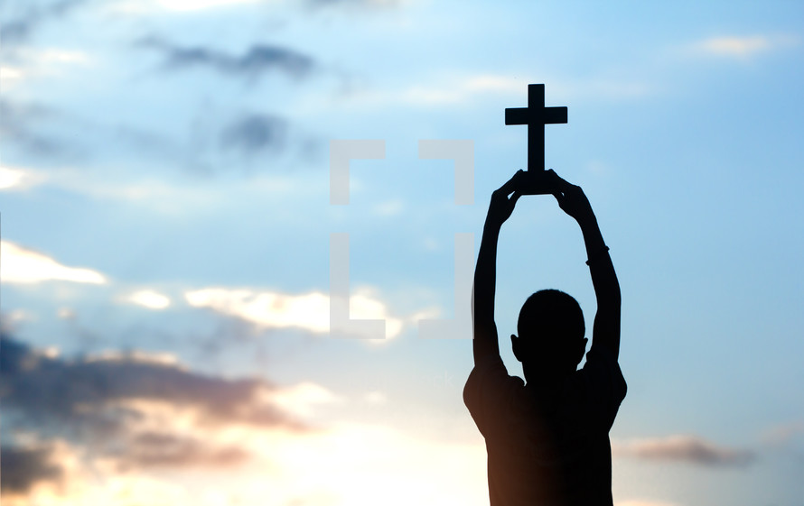 silhouette of a boy holding up a cross 