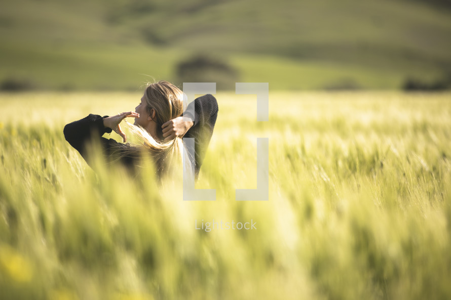 a woman putting her hair in a ponytail standing in a field of wheat 