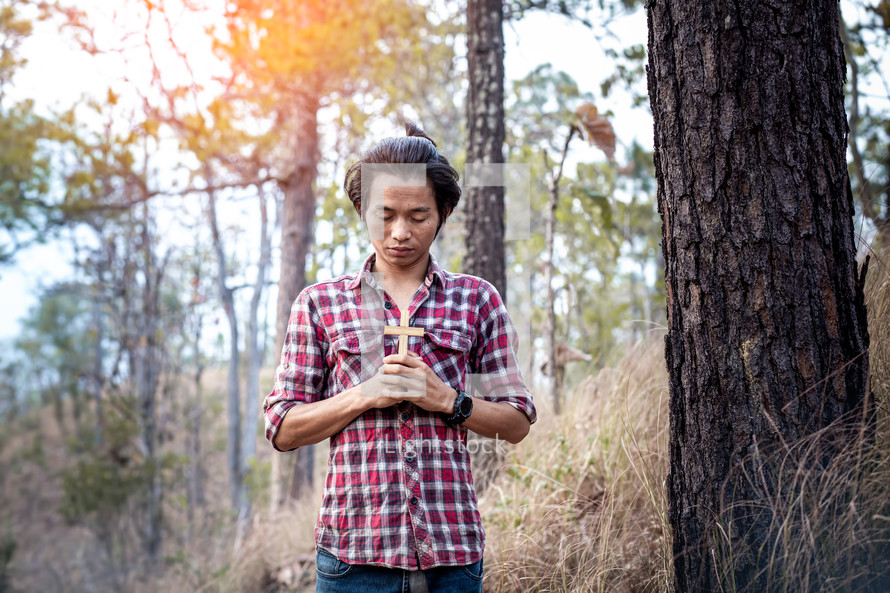 a man standing in a forest holding a cross praying 