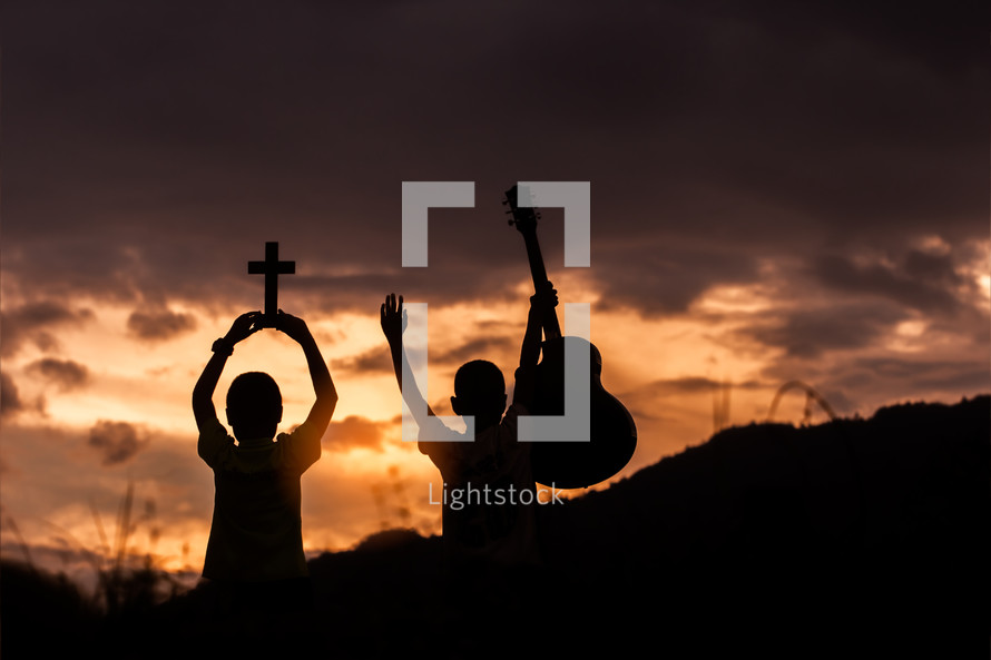 silhouettes of two boys at sunset one with a guitar and the other with a cross 