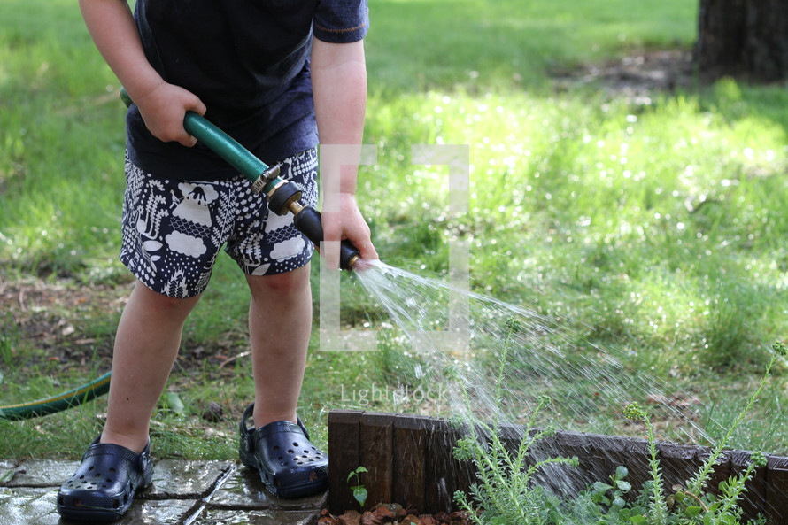 a toddler watering plants with a hose 