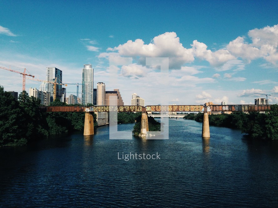A railroad bridge over a river with city skyscrapers in the background.