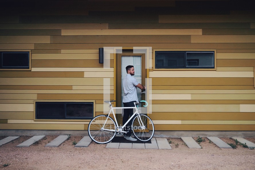 A man with a bicycle unlocks a door.