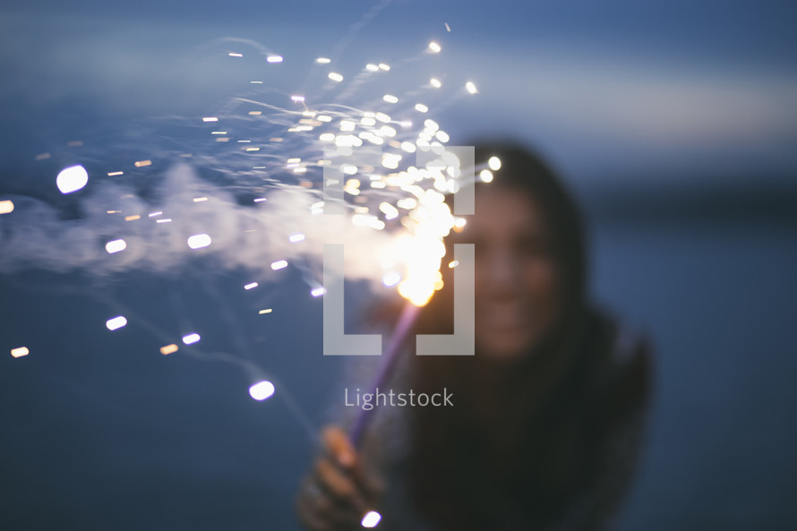 A woman holding a fiery sparkler.