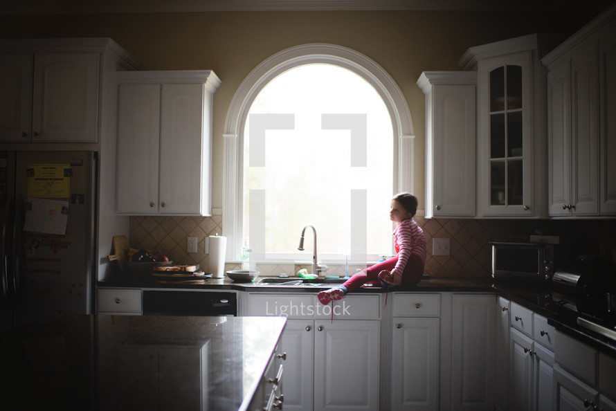 a little girl looking out a window sitting on a kitchen countertop 