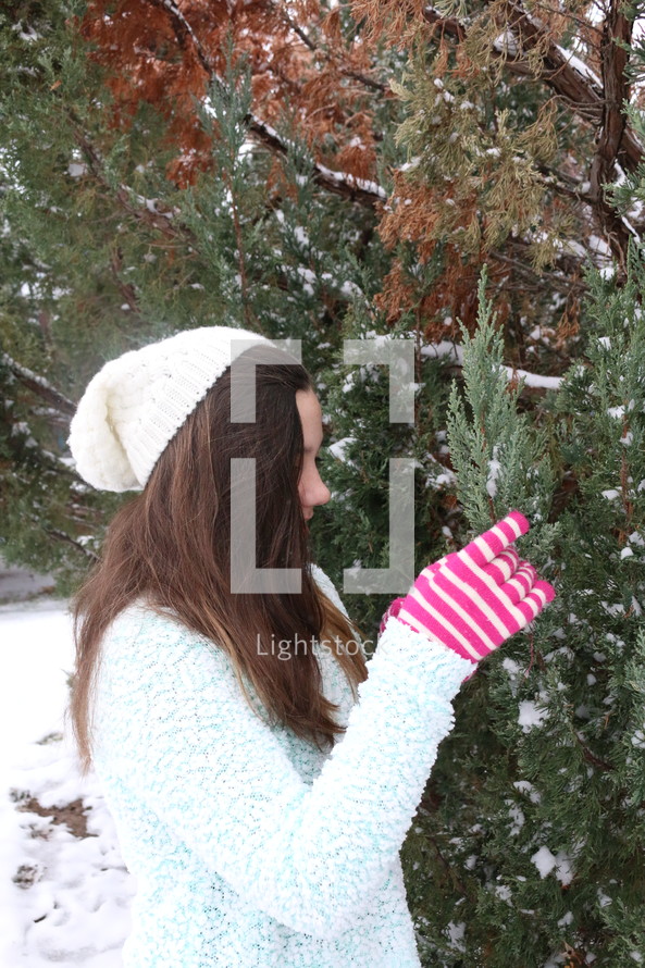 teen girl touching snow on bush with gloves on 