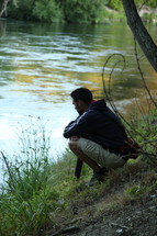 man squatting on a river bank