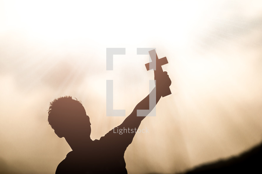 hand holding up a cross with sunlight at sunset in the background