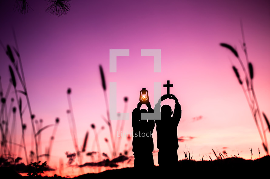 Two children holding oil lamp and cross with light sunset background 