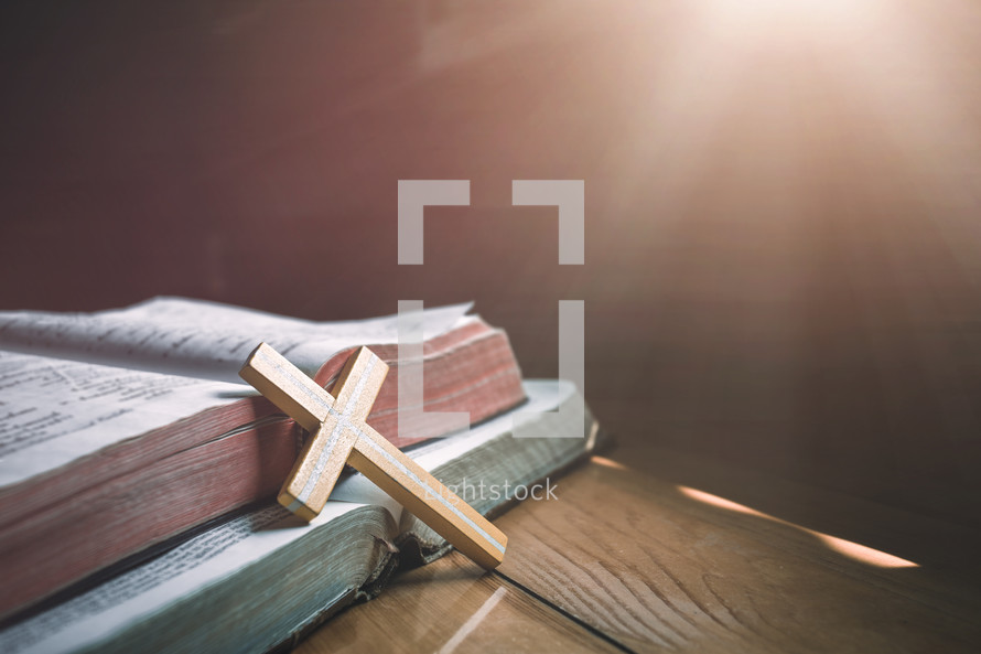 wooden cross leaning against open Bibles 