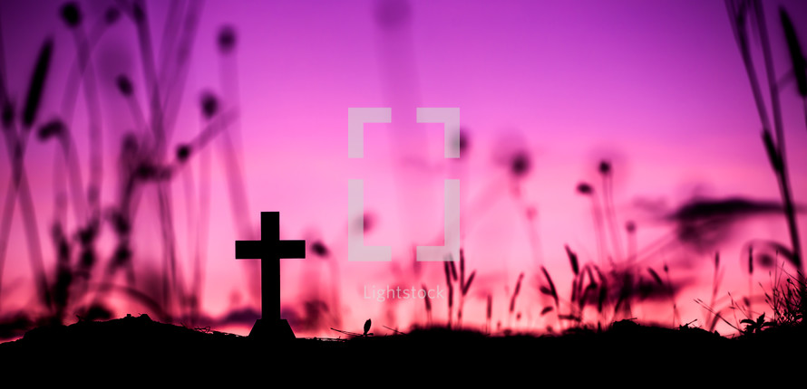 cross silhouette in a field at sunset against a purple sky 