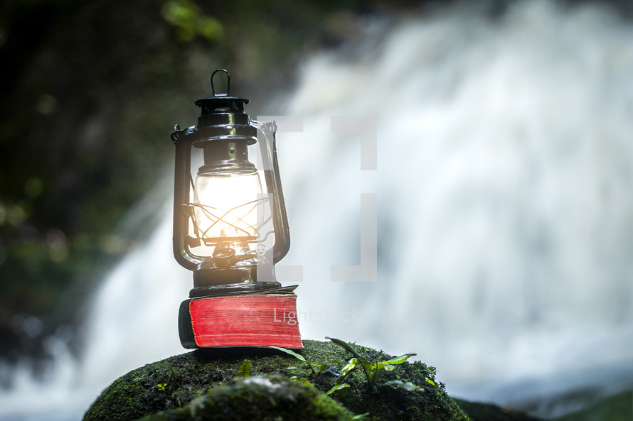 a lantern on a mossy rock in front of a waterfall 