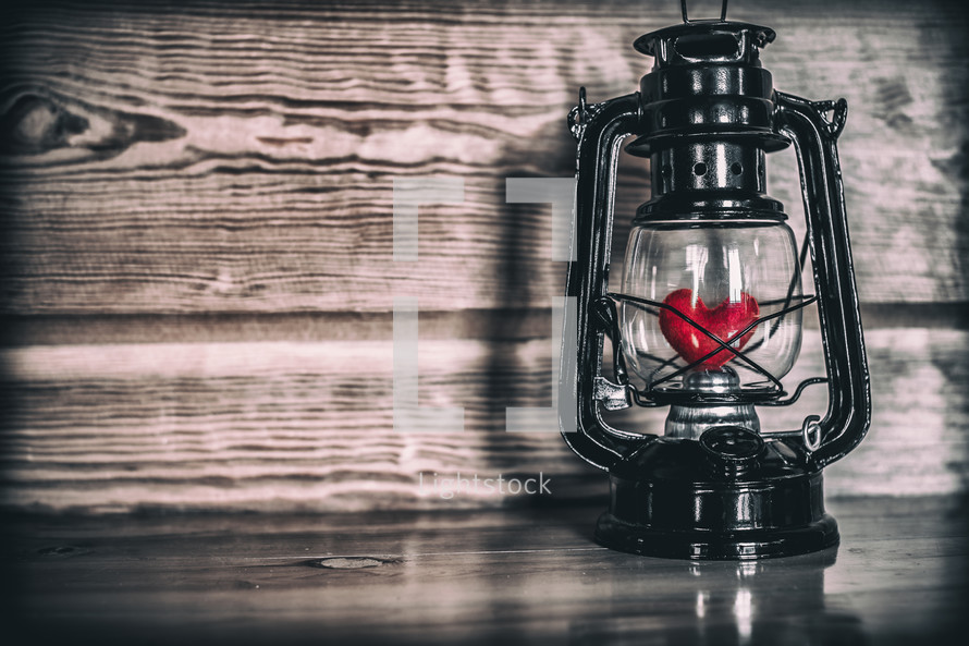 a red heart in a lantern against a wood background 