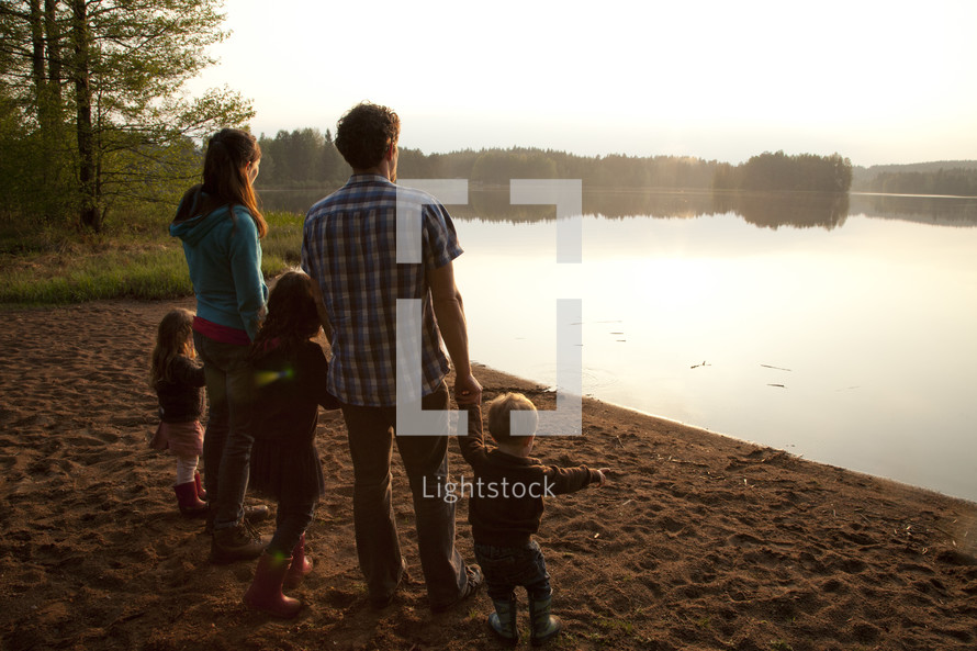 a young family standing on a lake shore holding hands in fall 